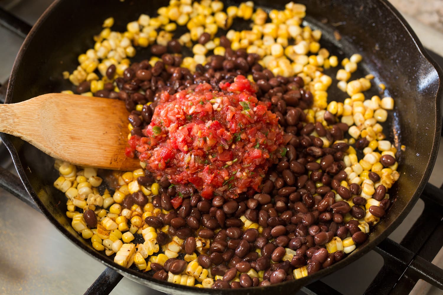 Adding black beans and salsa to corn.