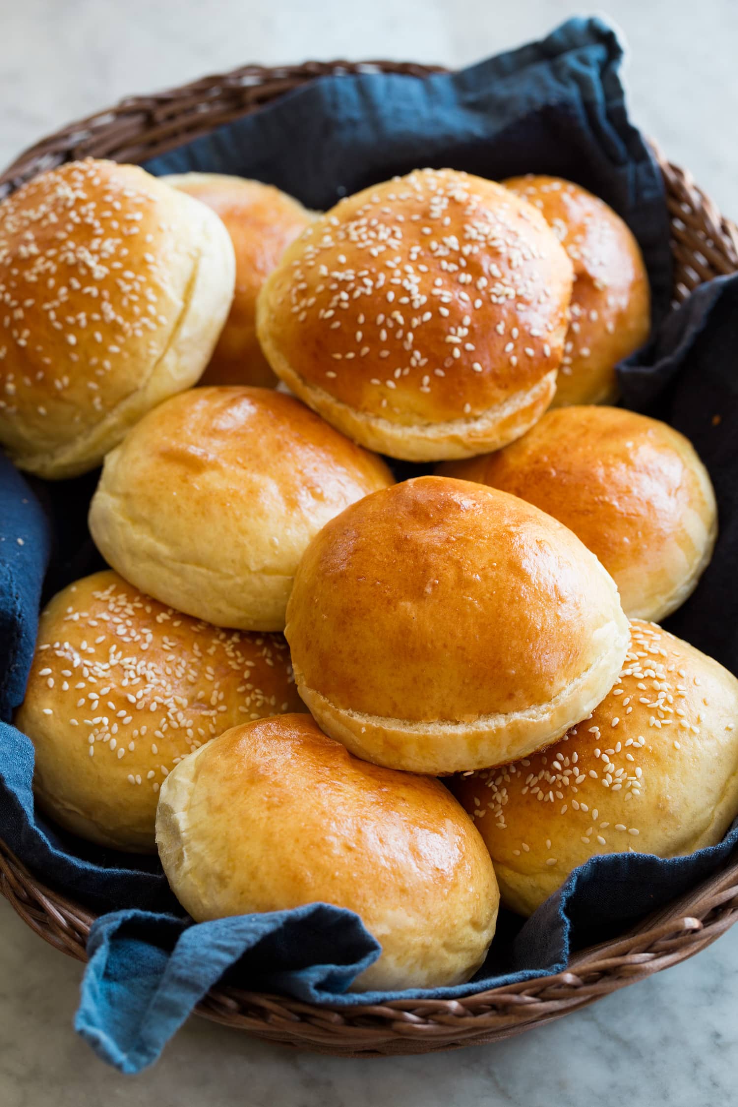 Homemade hamburger buns shown in a basket with a blue cloth.