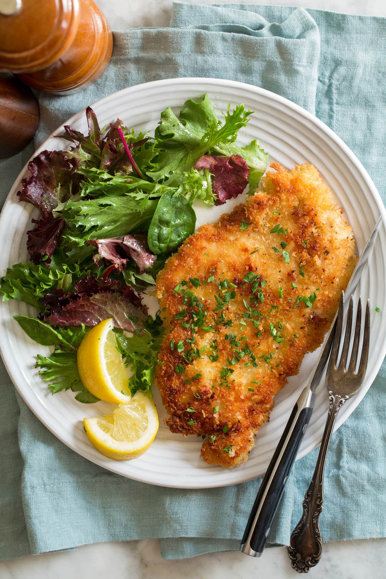 Chicken schnitzel shown served with lemons and a spring salad.