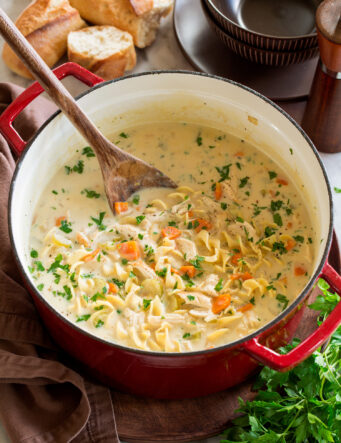 Pot full of homemade creamy chicken noodle soup served with a side of bread.