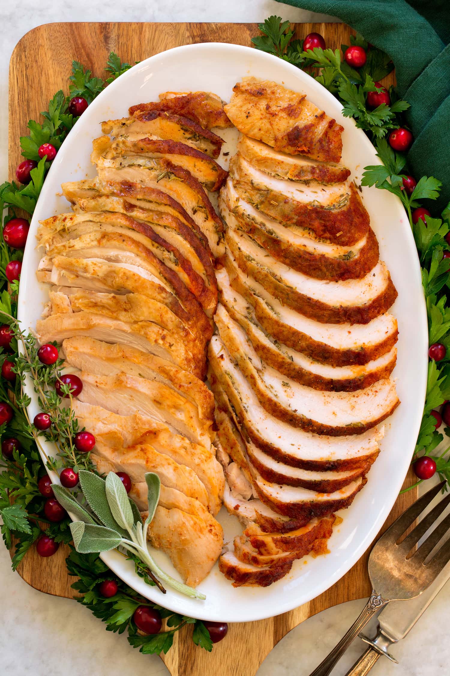Crockpot Turkey Breast shown sliced on an oval platter with green herbs and fresh cranberries decorating sides.