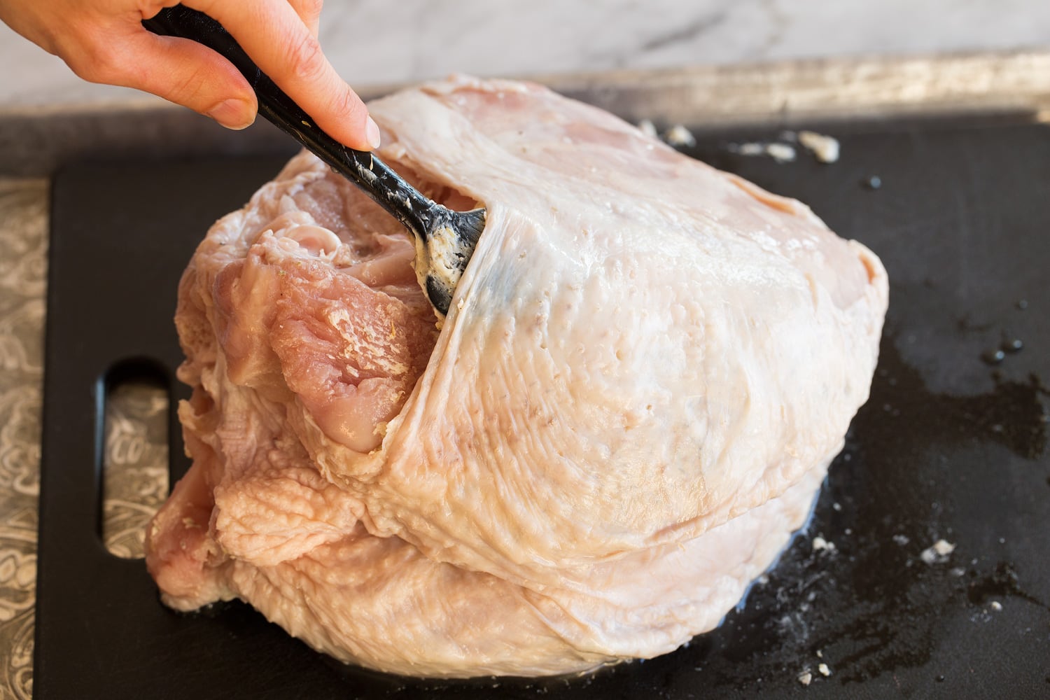 Adding butter herb mixture to a raw turkey breast under skin.