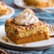 Single slice of pumpkin dump cake shown decorated with a swirl of whipped cream and cinnamon.