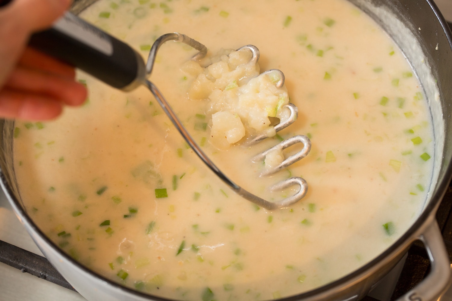 Mashing potatoes in pot of soup.
