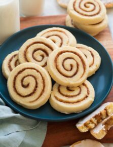 Cinnamon roll cookies piled on a blue plate on a wooden surface.