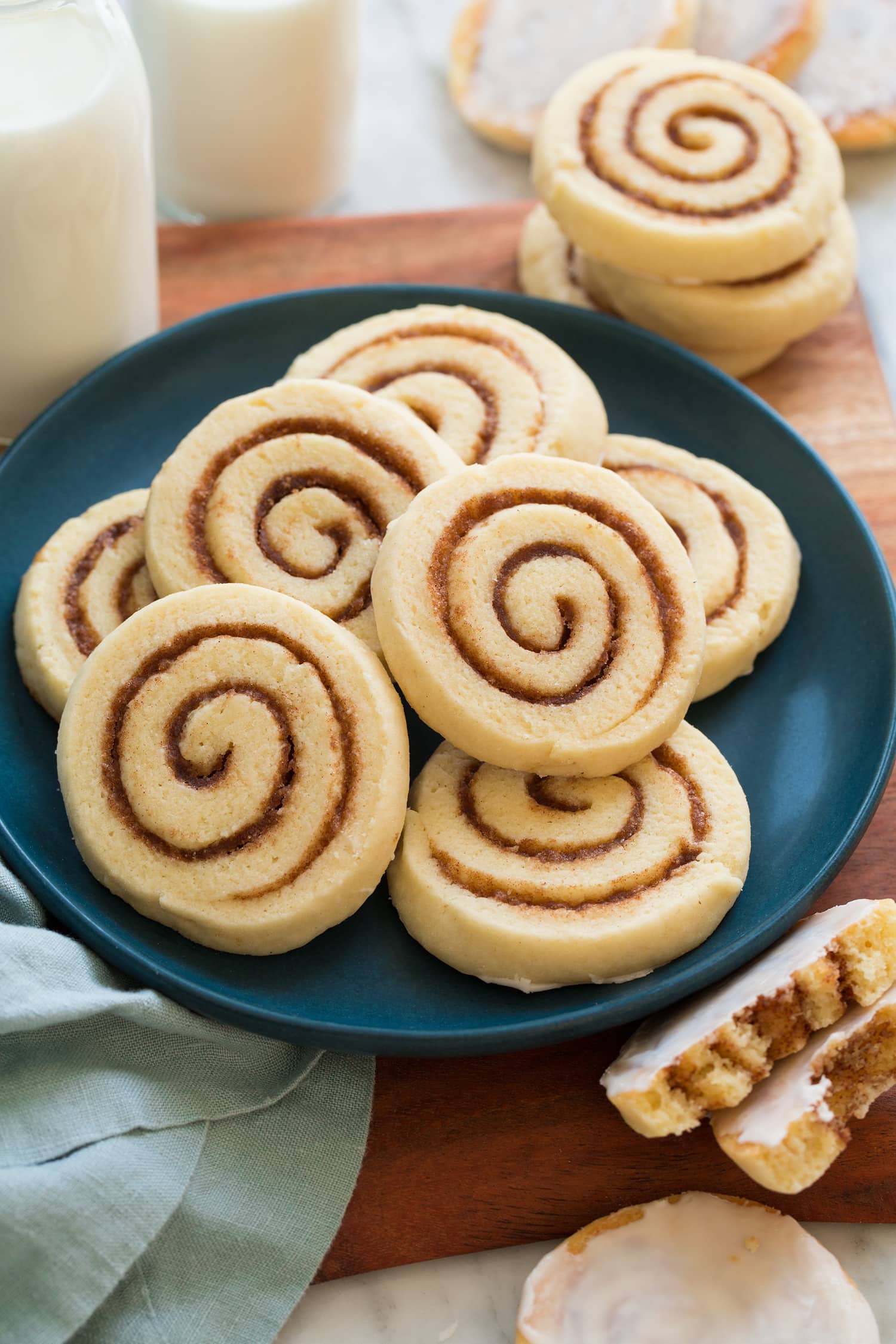 Cinnamon roll cookies piled on a blue plate on a wooden surface.