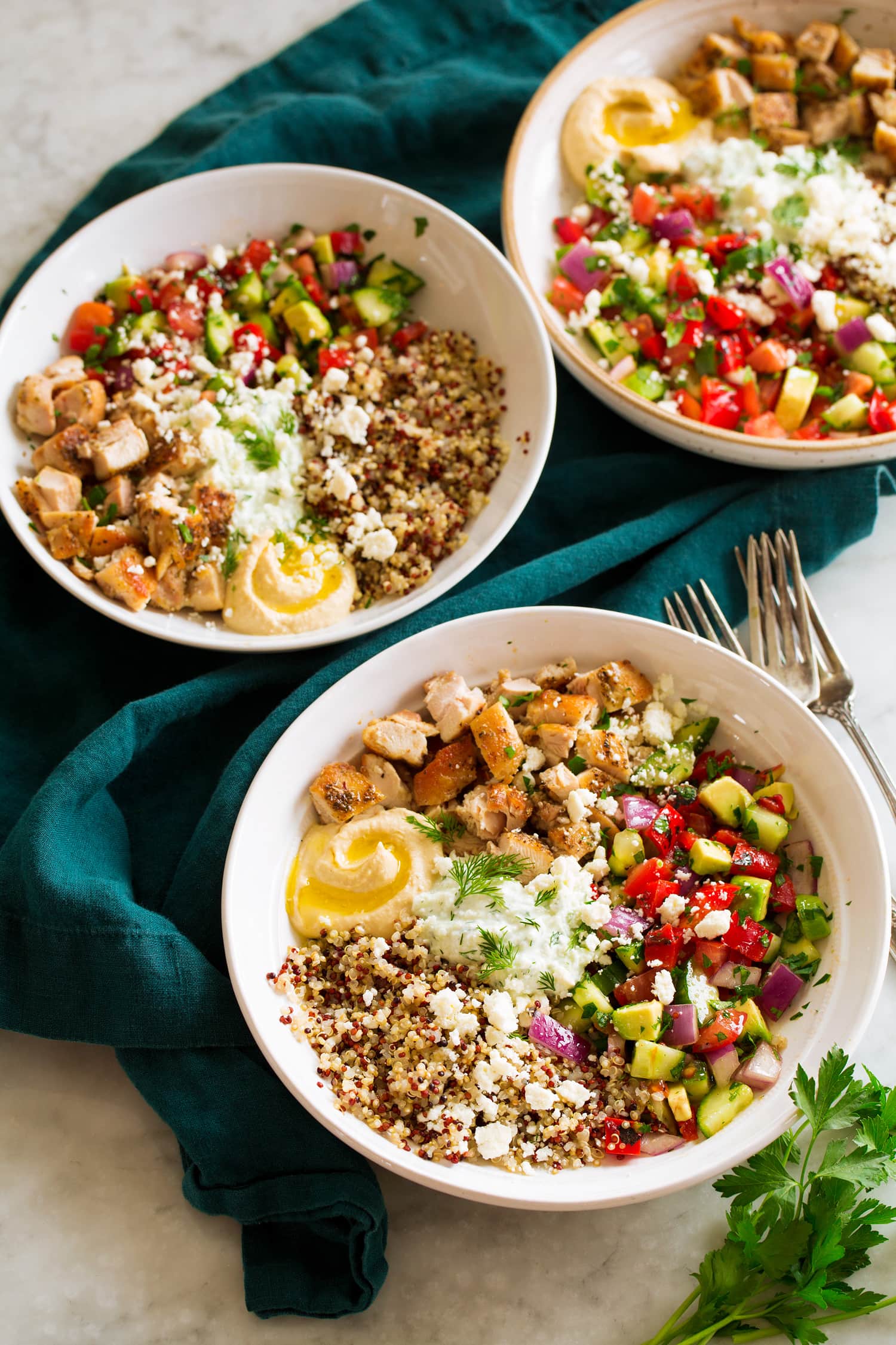 Three greek chicken bowls with grains and veggies.
