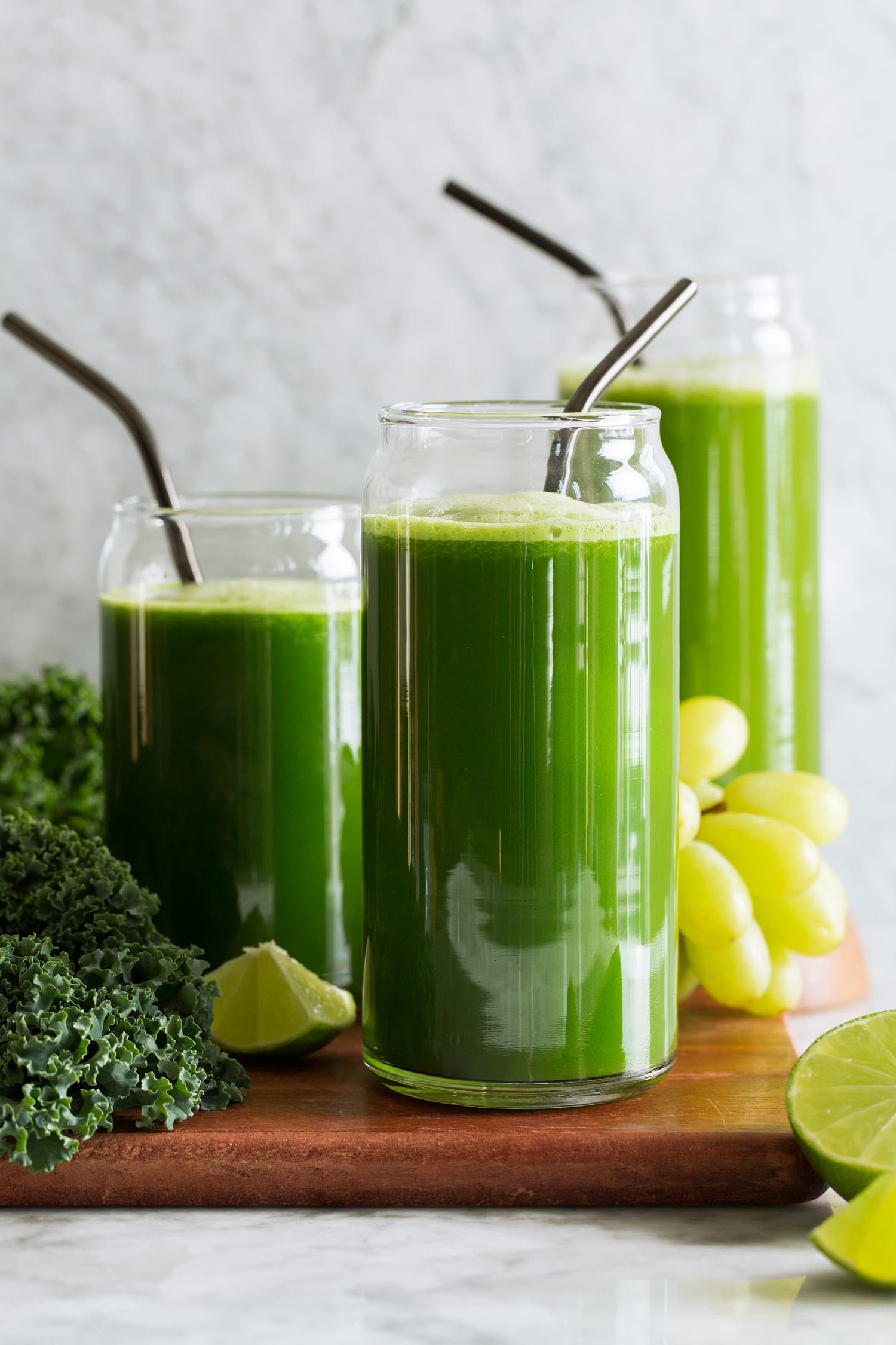 Three servings of green juices made with different greens including spinach, romaine lettuce and kale. Also includes cucumber, grapes, apples, celery, broccoli, lime and ginger.