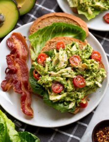 Avocado chicken salad shown on wheat bread with lettuce leaves and sliced grape tomatoes.