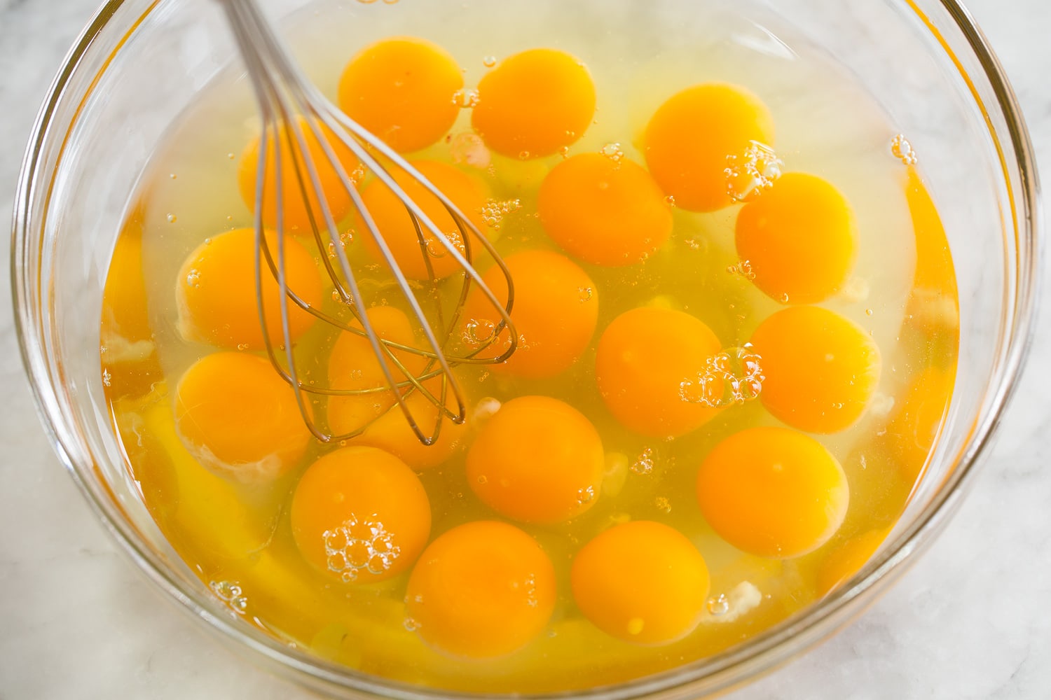 18 eggs in a glass mixing bowl being whisked together.