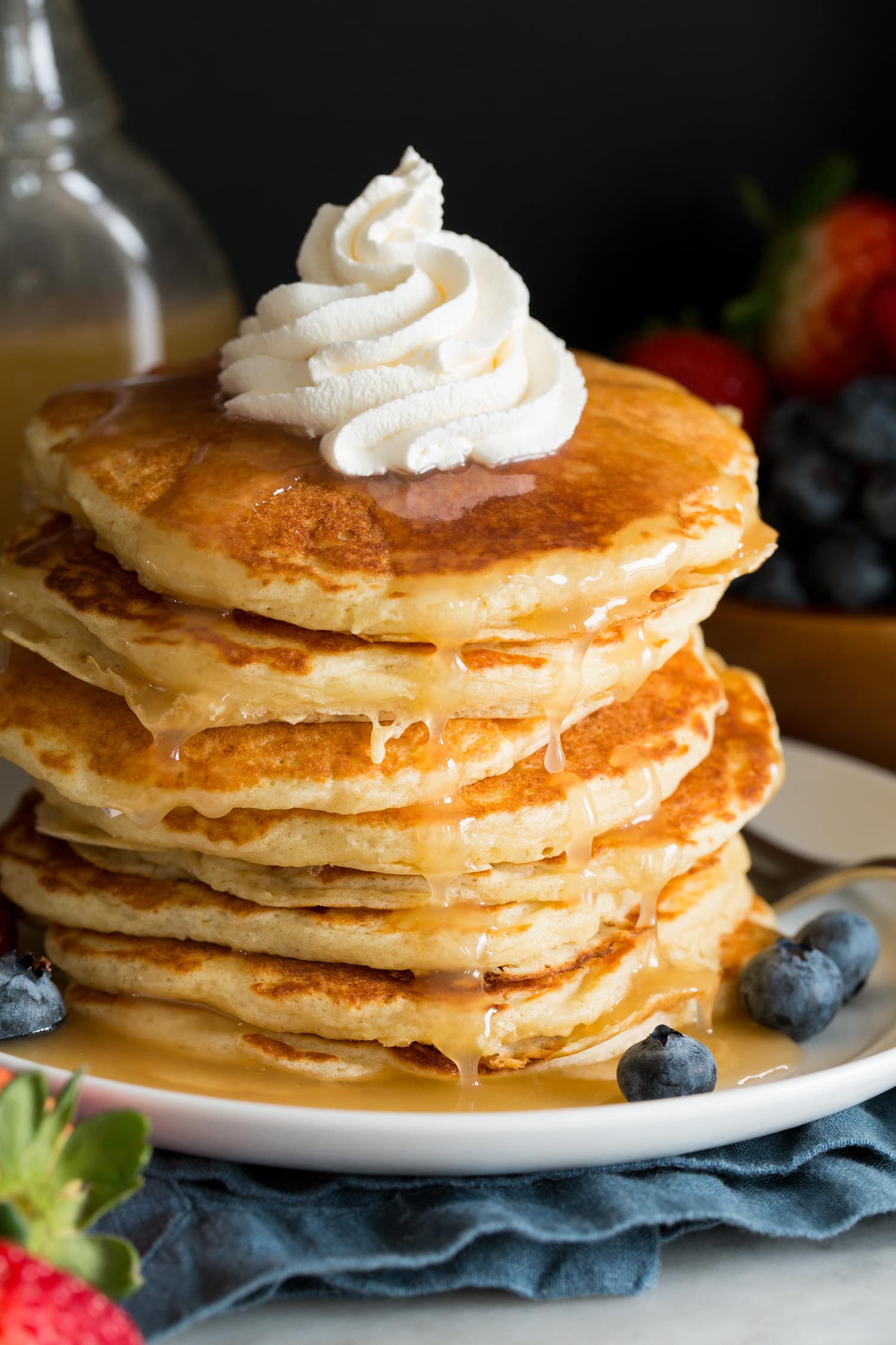 Stack of homemade buttermilk pancakes with buttermilk syrup drizzled over the top and whipped cream piped over.