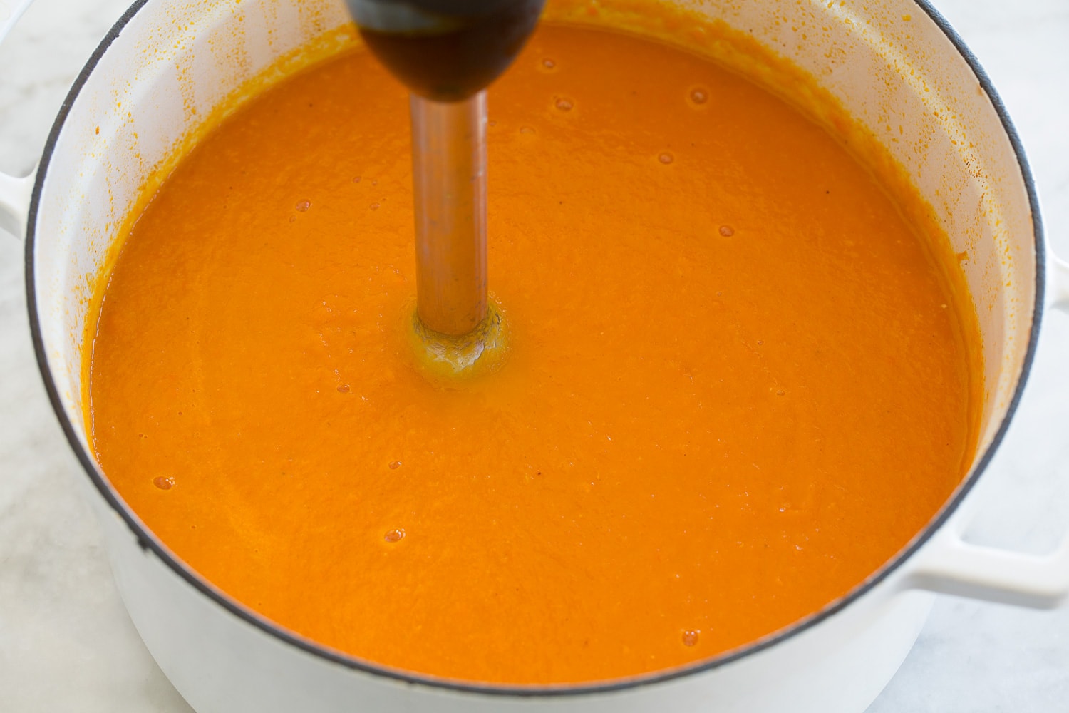 Carrot soup being processed with an immersion blender.