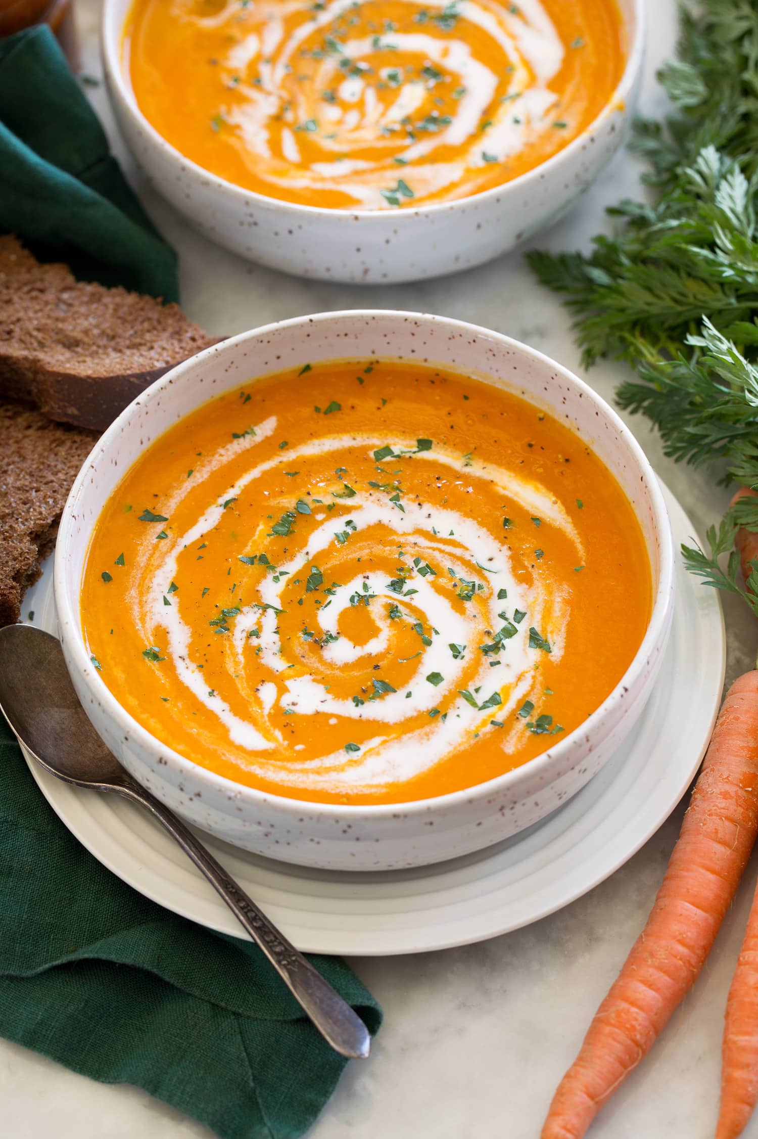 Single serving of carrot soup in a soup bowl with a second serving shown in the background.