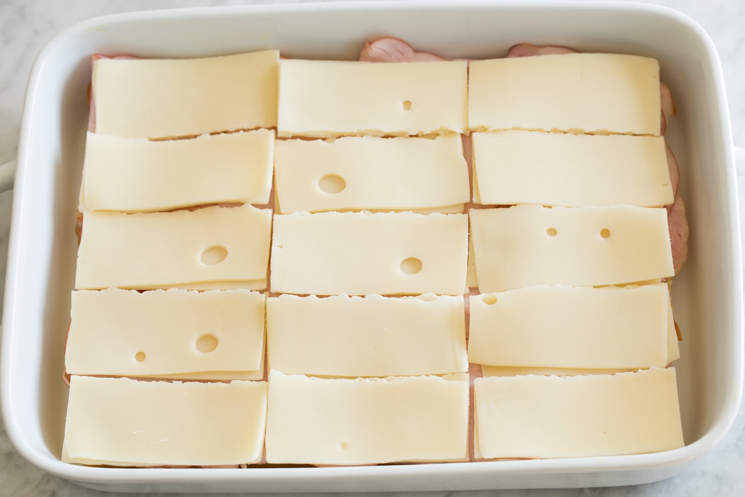 Layering swiss cheese over ham layer of sliders.