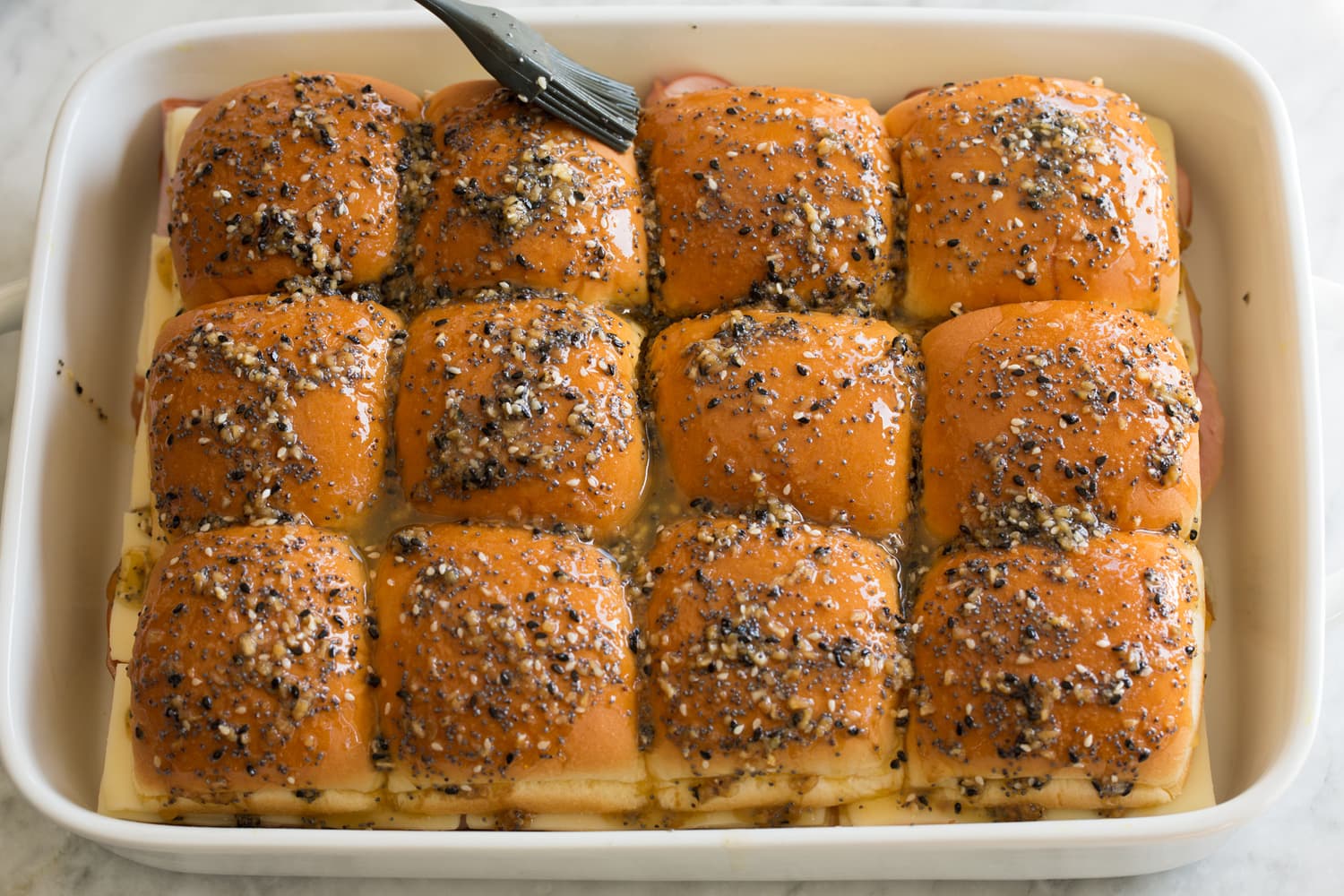 Spreading butter poppy seed mixture over rolls in casserole dish.