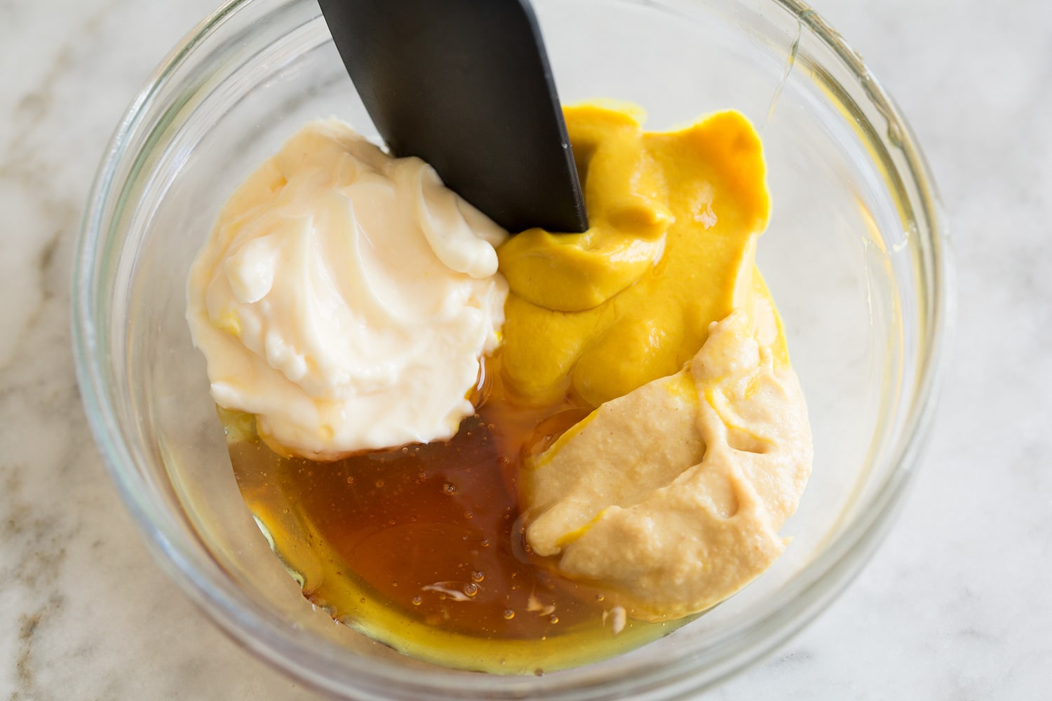 Making creamy honey mustard spread in glass mixing bowl.