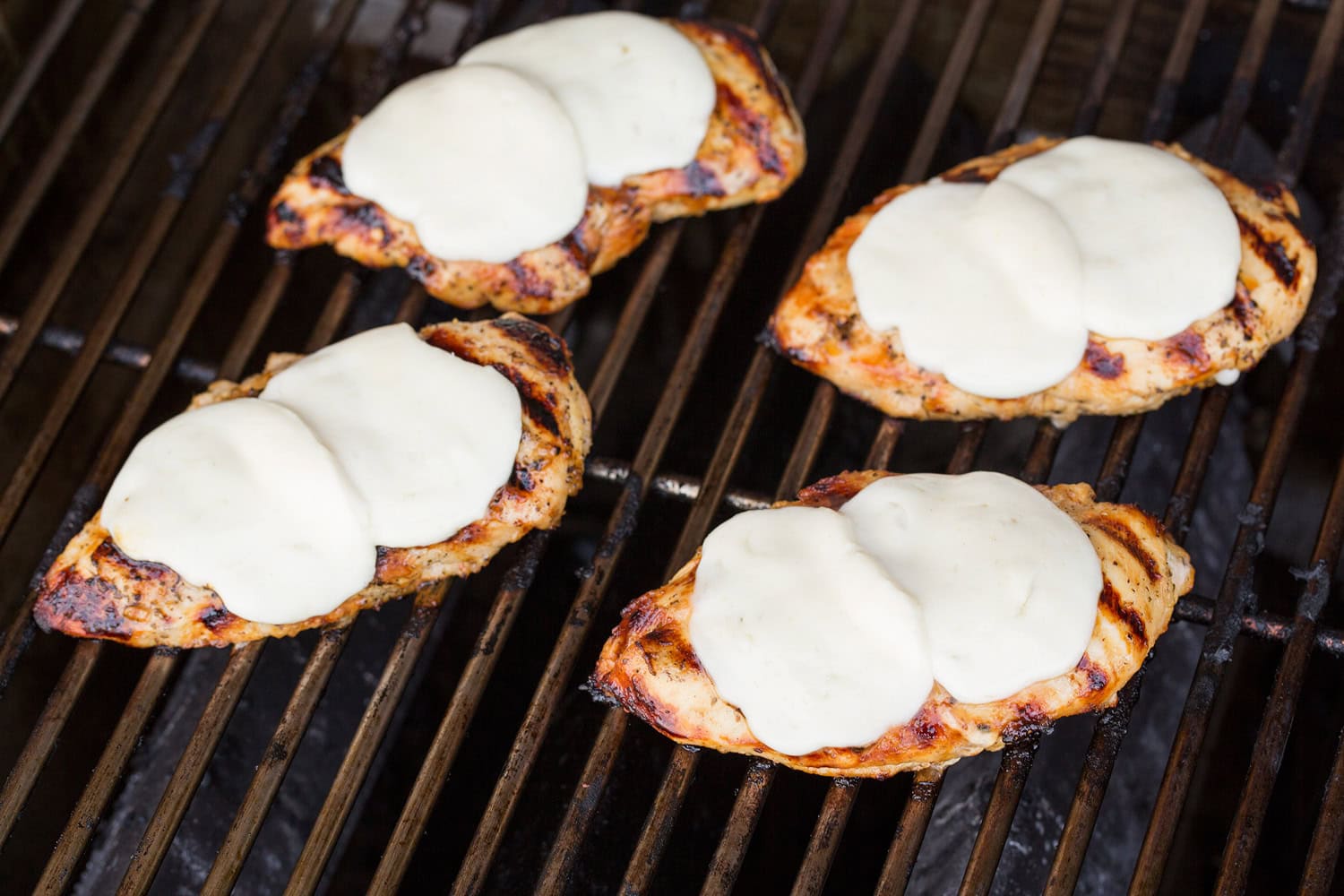 Mozzarella cheese melted over chicken breasts on grill.