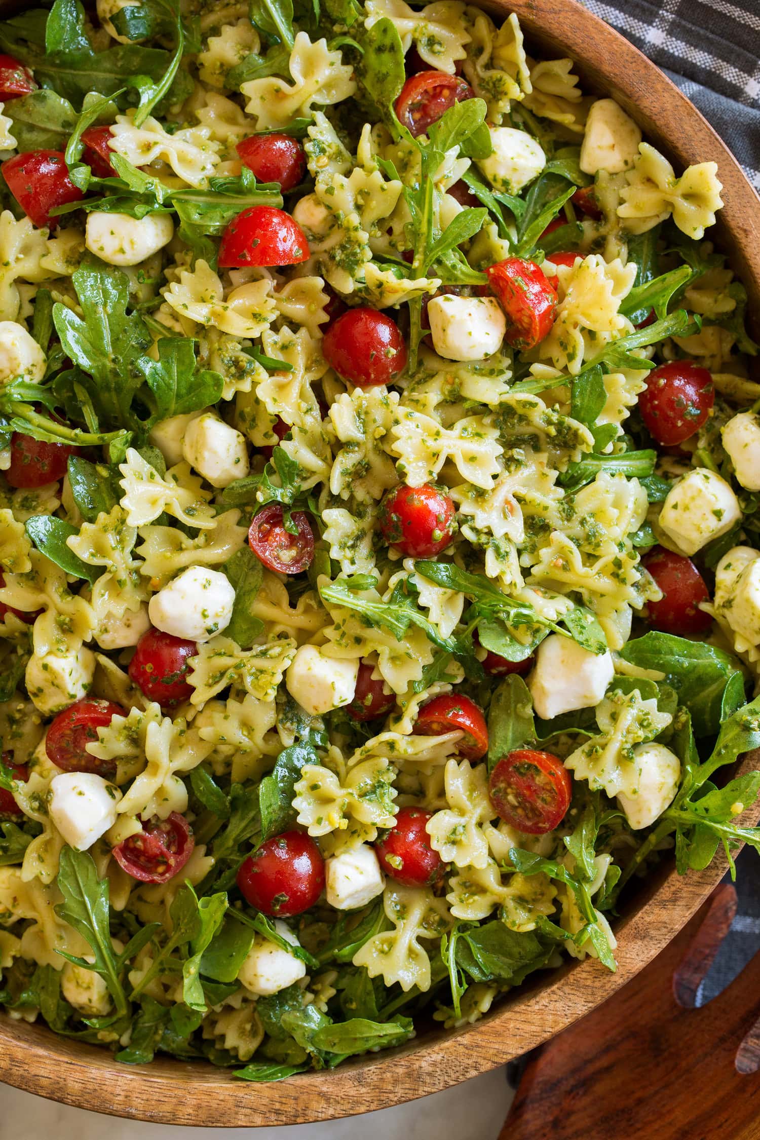 Close up photo of bowtie pasta salad with pesto, tomatoes, arugula and fresh mozzarella.