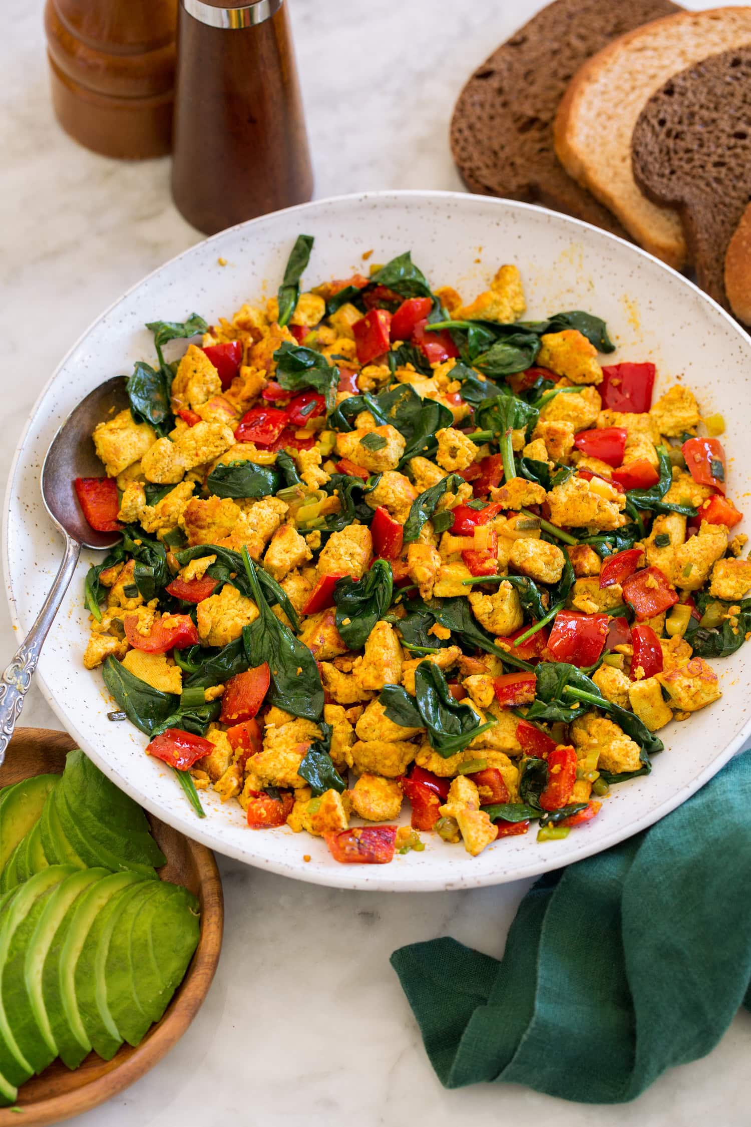 Tofu scramble in a white ceramic bowl over a marble surface with a green cloth to the side.