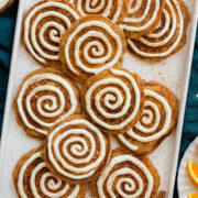 Cinnamon roll pancakes shown featuring cinnamon pancakes with a cream cheese swirl over pancakes. They are all laid out on a platter and shown from overhead.
