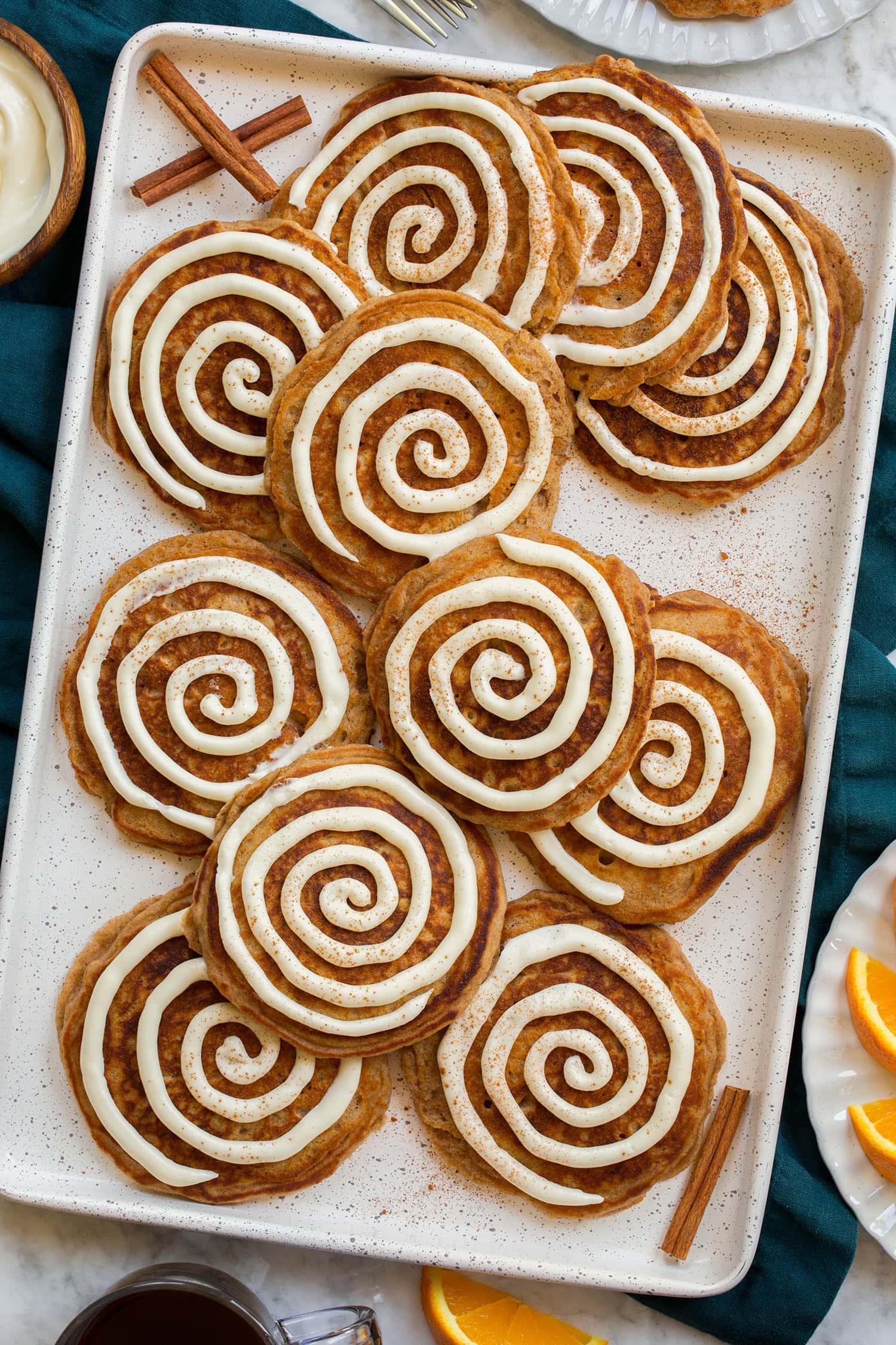 Cinnamon Roll Pancakes Cinnamon roll pancakes shown featuring cinnamon pancakes with a cream cheese swirl over pancakes. They are all laid out on a platter and shown from overhead.