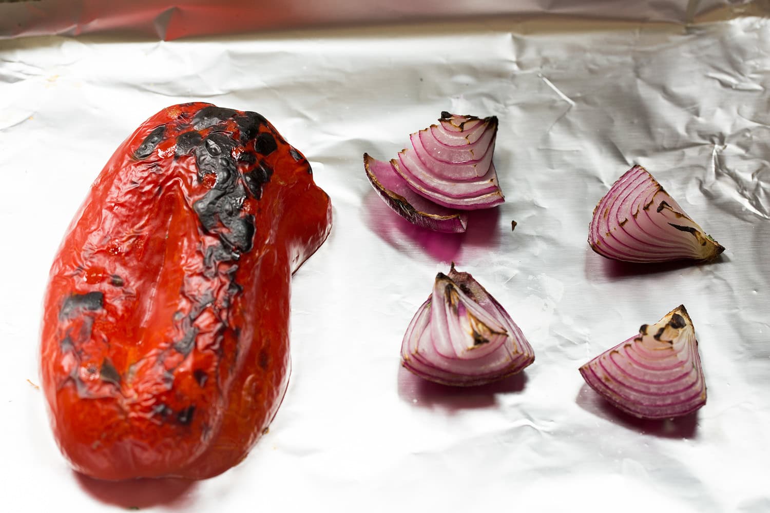 Ant folijos išklotos kepimo skardos skrudintos pipirų ir raudonojo svogūno.