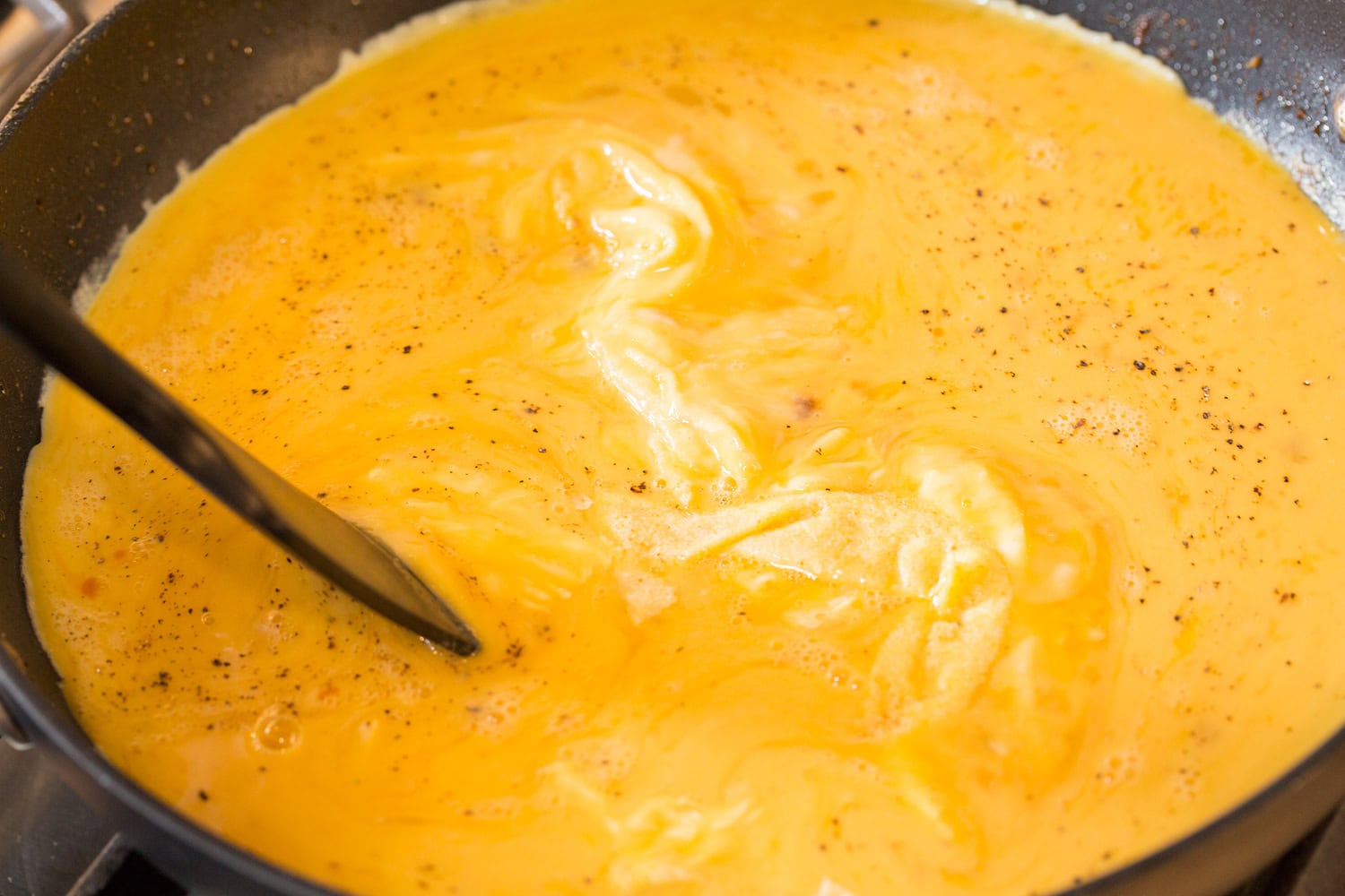 Maišant plaktus kiaušinius nelipniai keptuvėje su mentele.