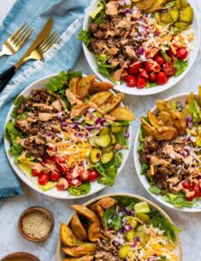 Four burger bowls shown from overhead on a marble surface with a blue cloth to the side.