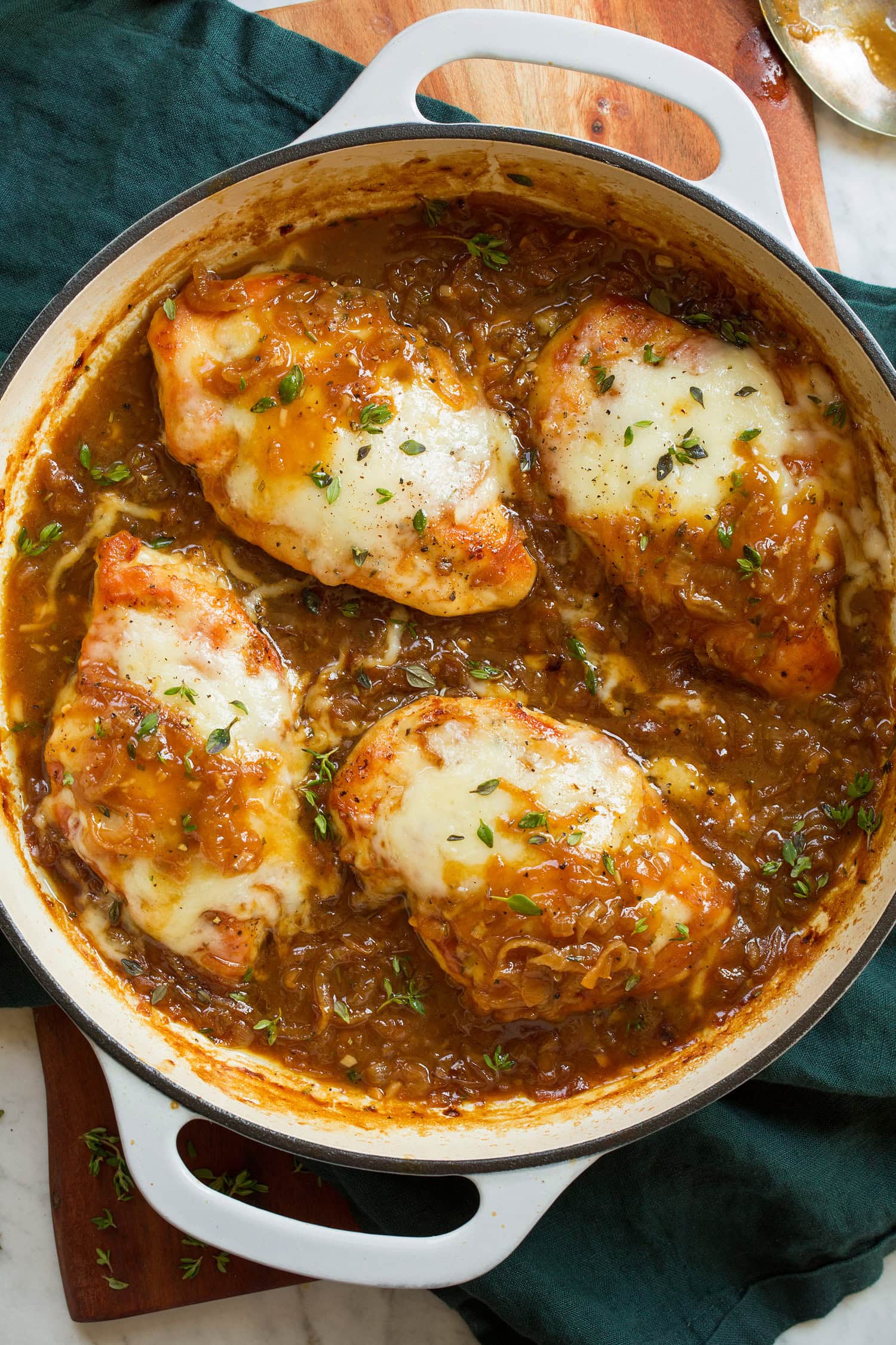 Four pieces of French onion chicken with Swiss cheese and herbs in a skillet.