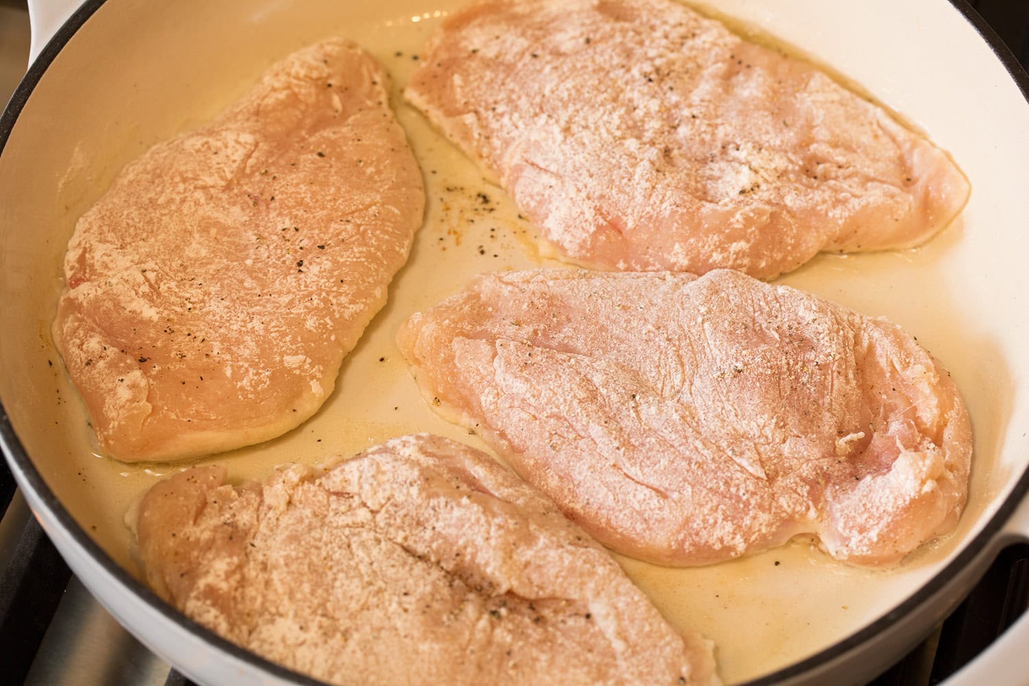 Flour coated chicken breasts shown raw in skillet before cooking.