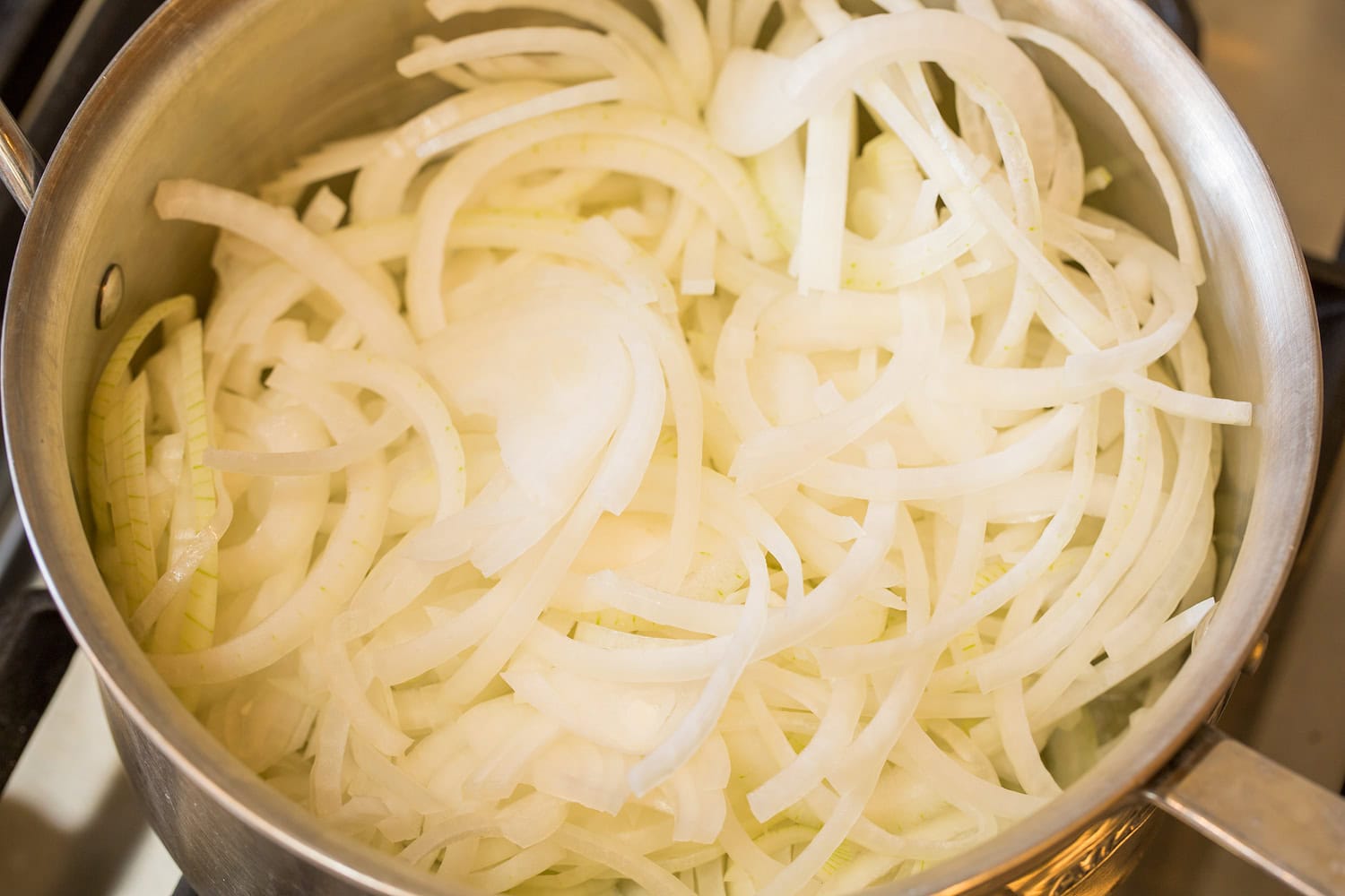 Sliced onions in saucepan shown raw. 