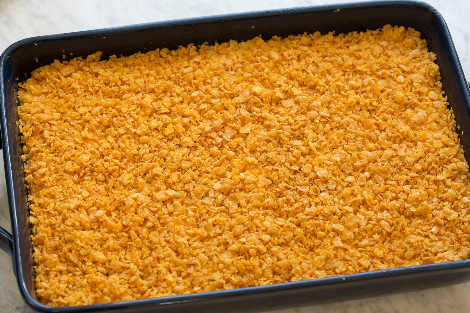 Funeral Potatoes Cornflake topping spread over hash brown mixture in baking dish.