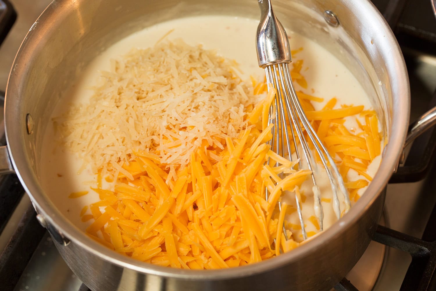 Cheddar and parmesan added to white sauce in saucepan.
