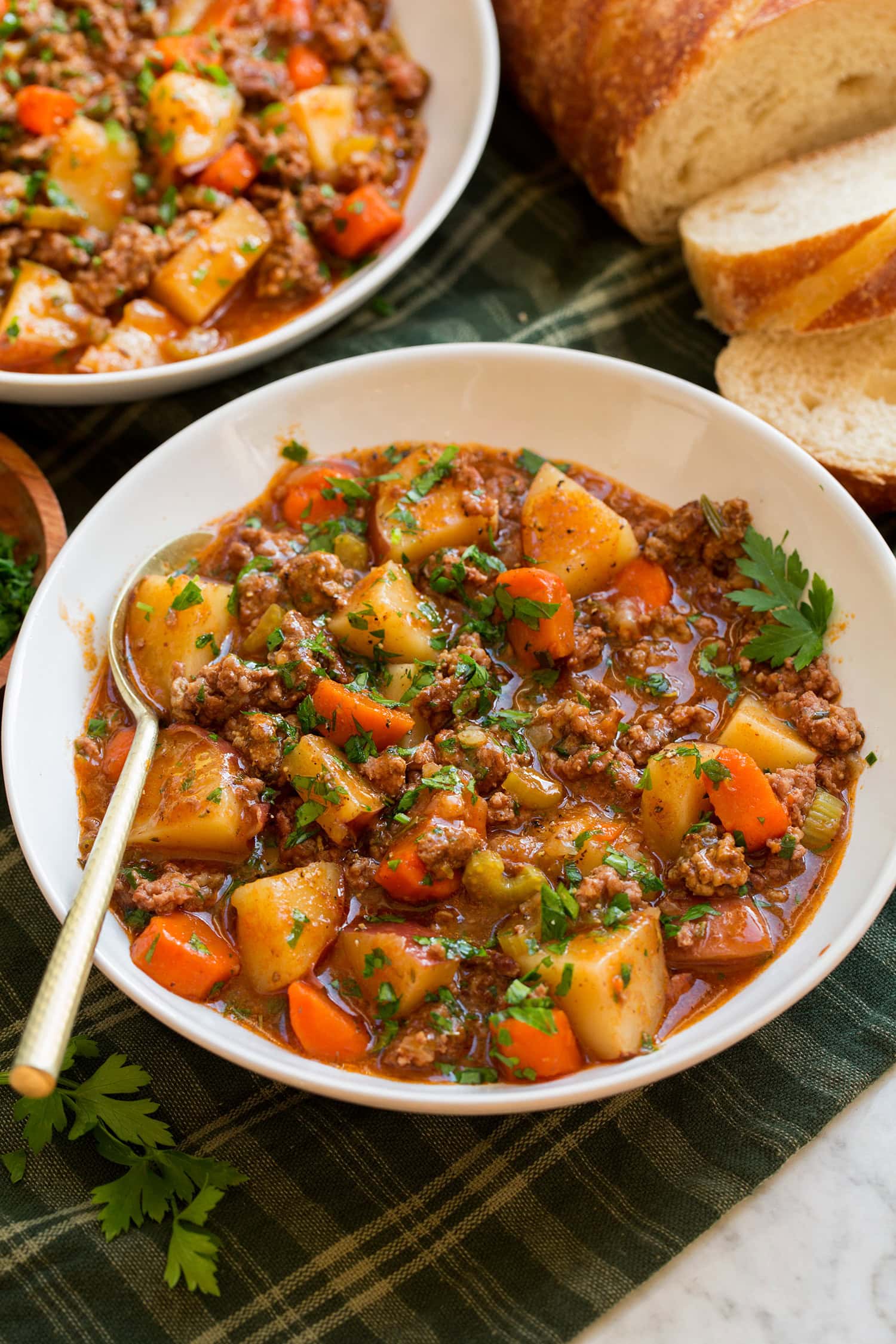 Ground beef stew shown in a white serving bowl over a green plaid cloth.