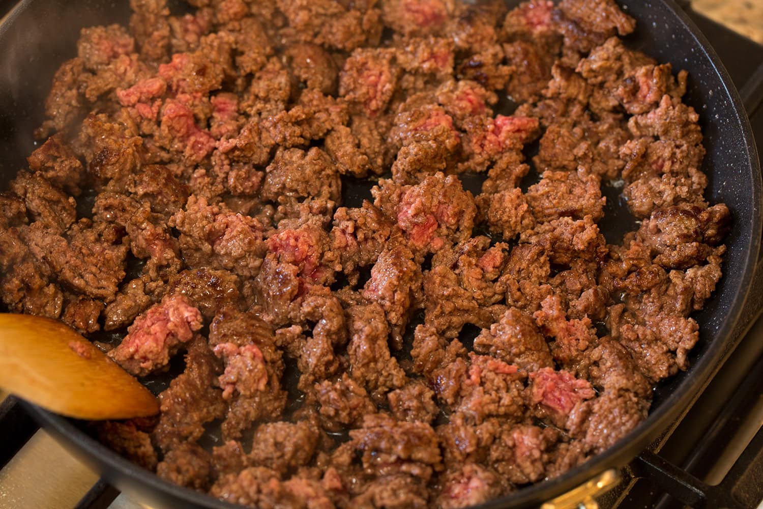 Crumbled nearly cooked through ground beef in a skillet.