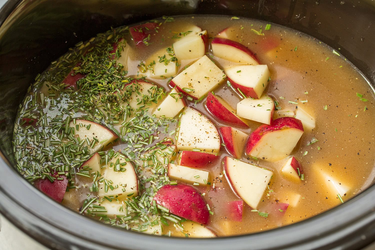 Potatoes, broth and herbs in a slow cooker.