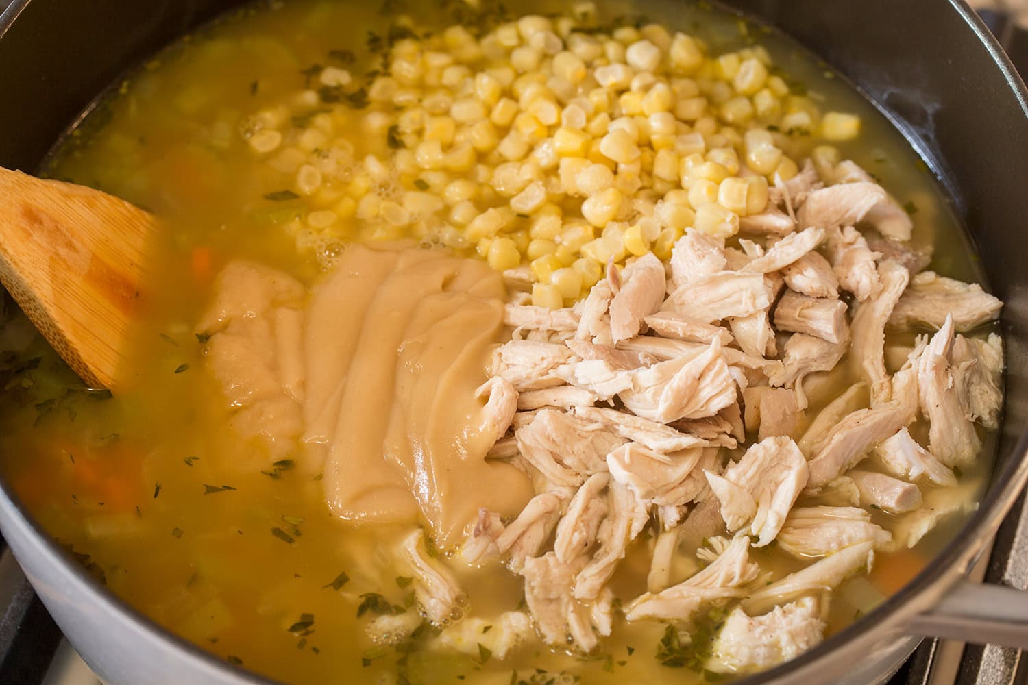 Corn, leftover turkey, and gravy added to soup in pot.