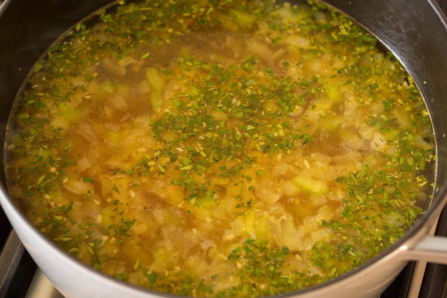 Turkey stock and herbs added to vegetables in pot, simmering.