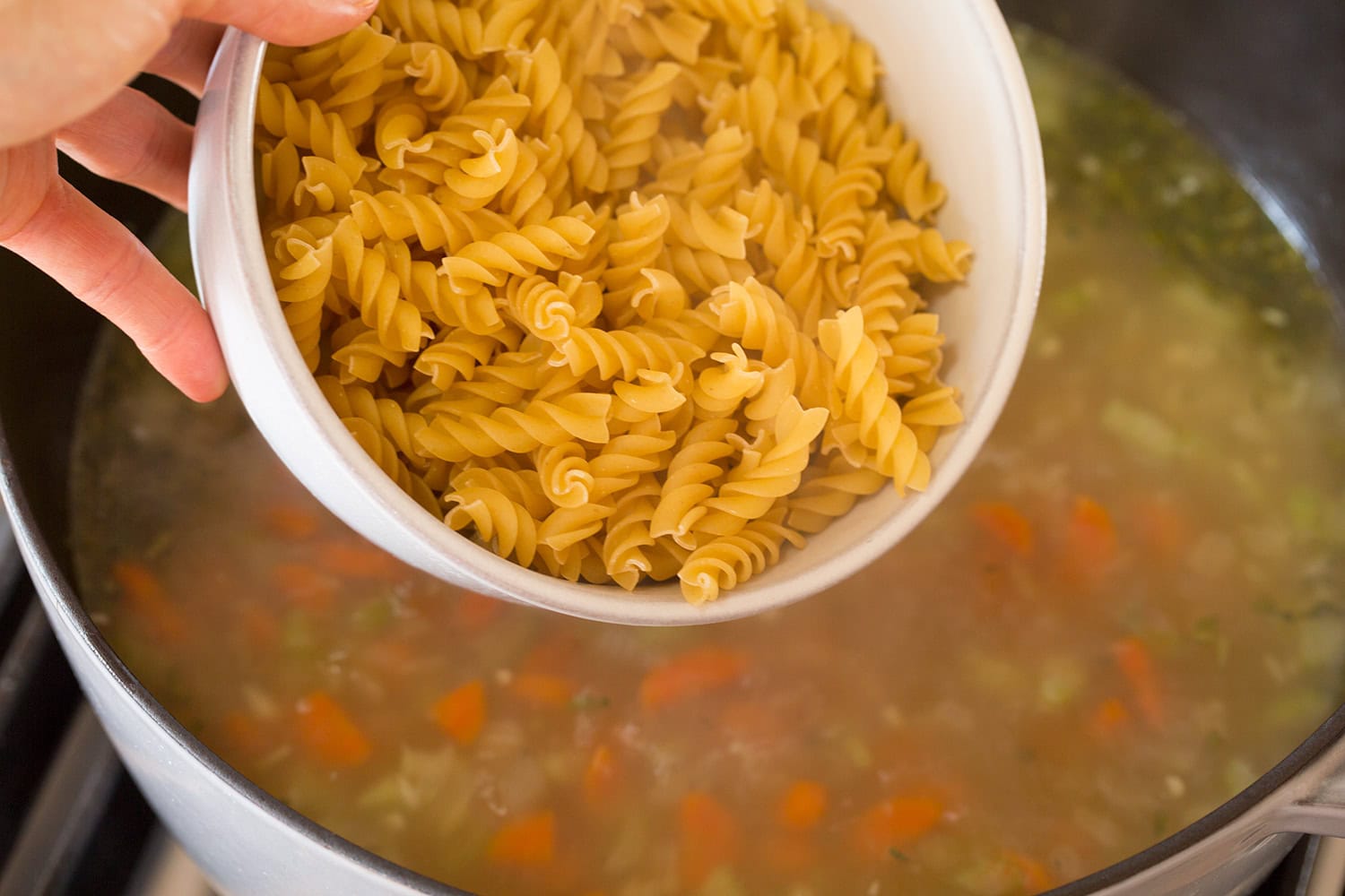 Noodles being added to stock in pot.