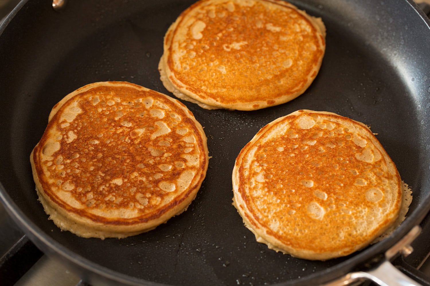 Protein pancakes flipped and shown cooked on second side in skillet.