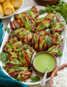 Grilled Peruvian chicken on a white platter, chicken is drizzled in aji verde sauce a Peruvian green cilantro sauce.