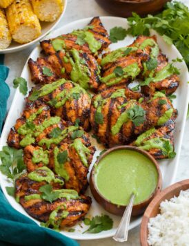 Grilled Peruvian chicken on a white platter, chicken is drizzled in aji verde sauce a Peruvian green cilantro sauce.