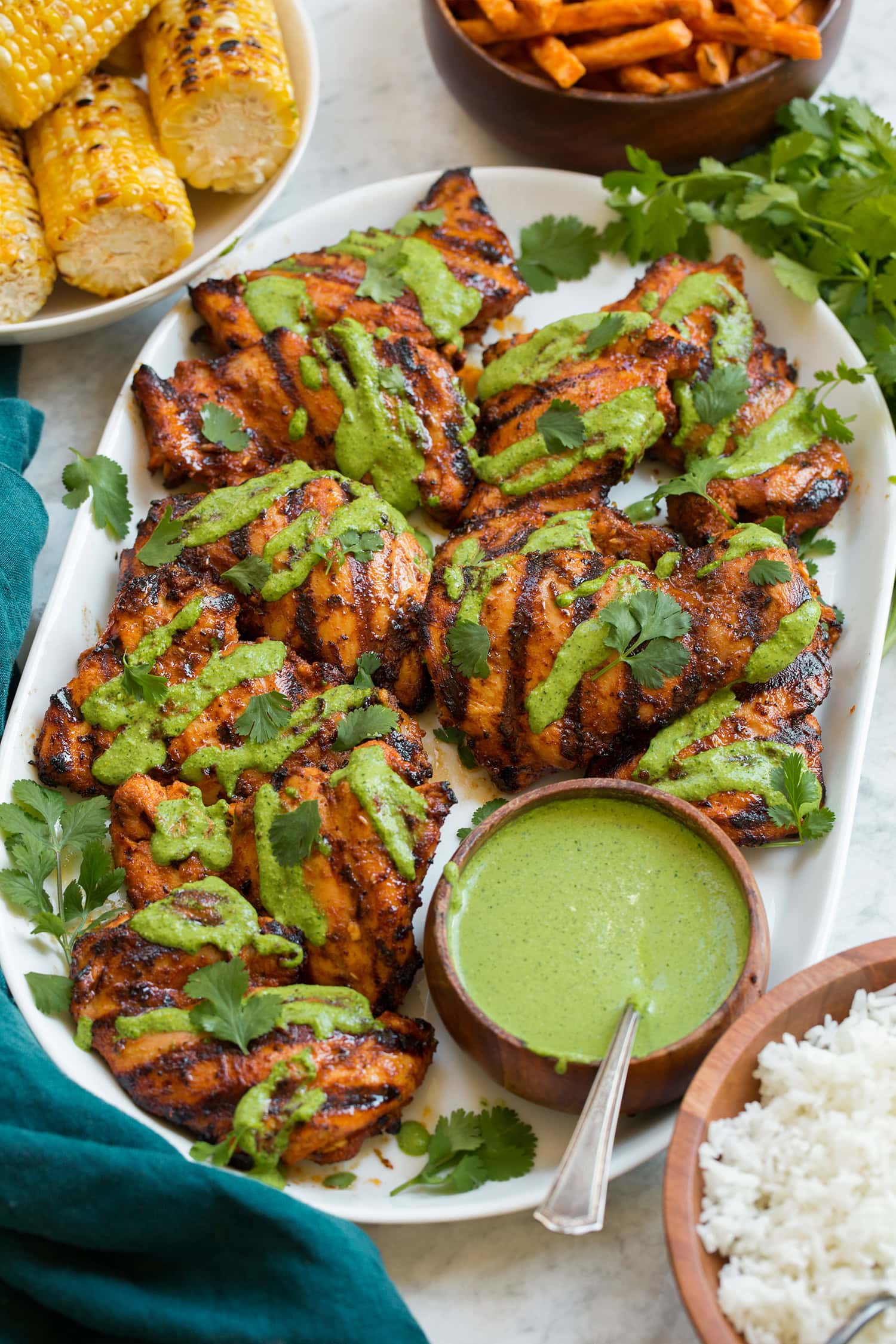 Grilled Peruvian chicken on a white platter, chicken is drizzled in aji verde sauce a Peruvian green cilantro sauce.