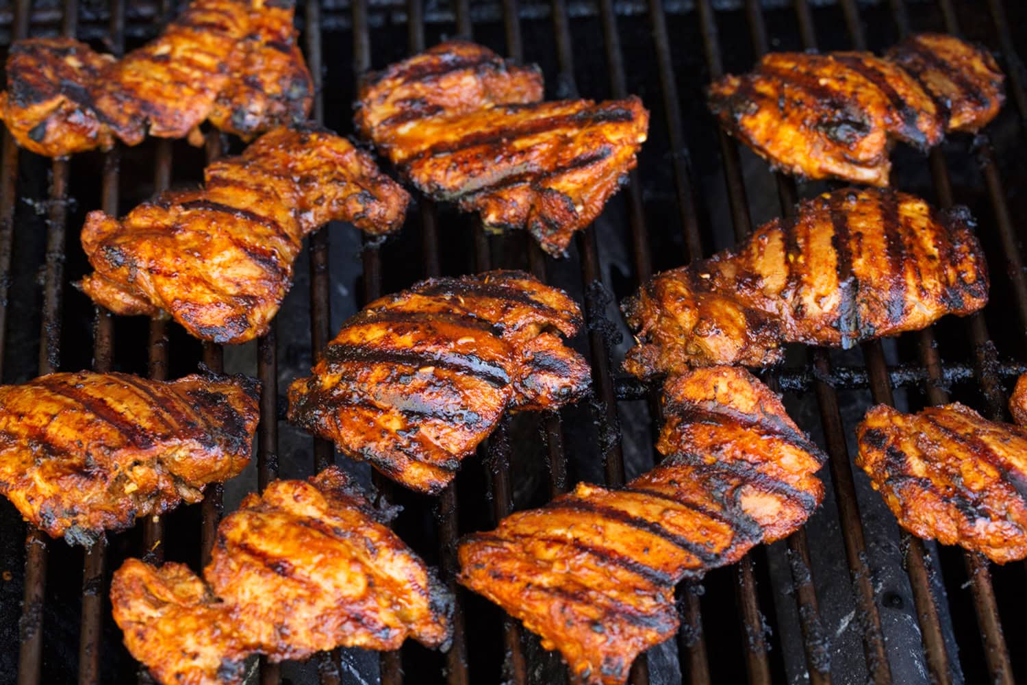 Peruvian chicken thighs shown fully cooked on grill grates.