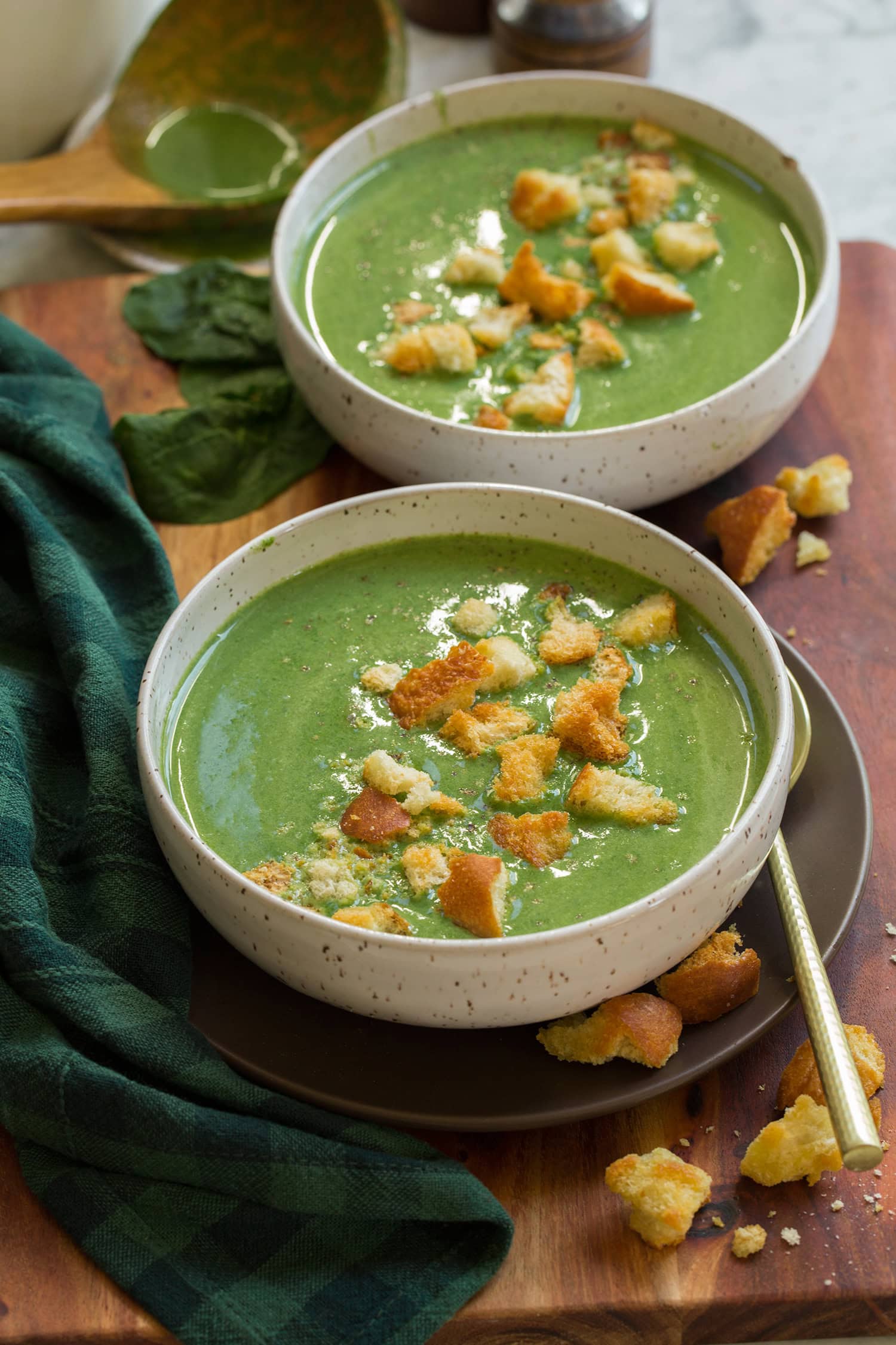Spinach Soup Two bowls of spinach soup sitting on brown plates with croutons to the side and a checkered blue and green decorative napkin.