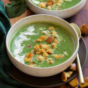 Spinach soup shown with cream, homemade croutons and parmesan cheese on top. Two servings shown in white bowls.