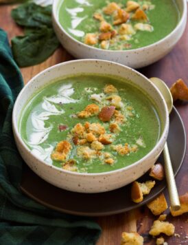 Spinach soup shown with cream, homemade croutons and parmesan cheese on top. Two servings shown in white bowls.