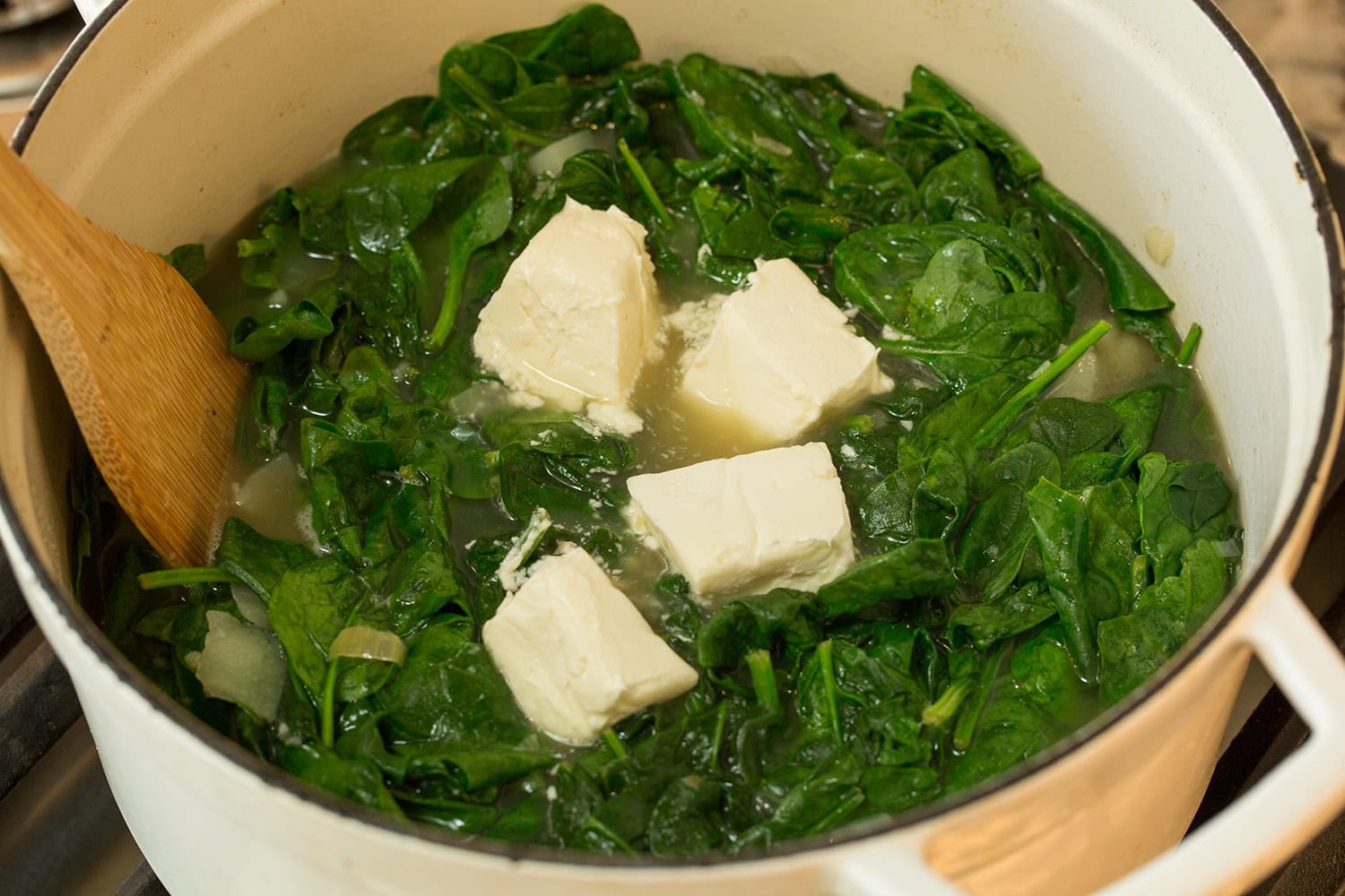 Spinach Soup Chunks of softened cream cheese added over wilted spinach in pot.