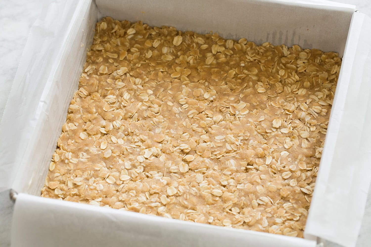 Oat crumb mixture pressed into a parchment paper lined square baking dish.