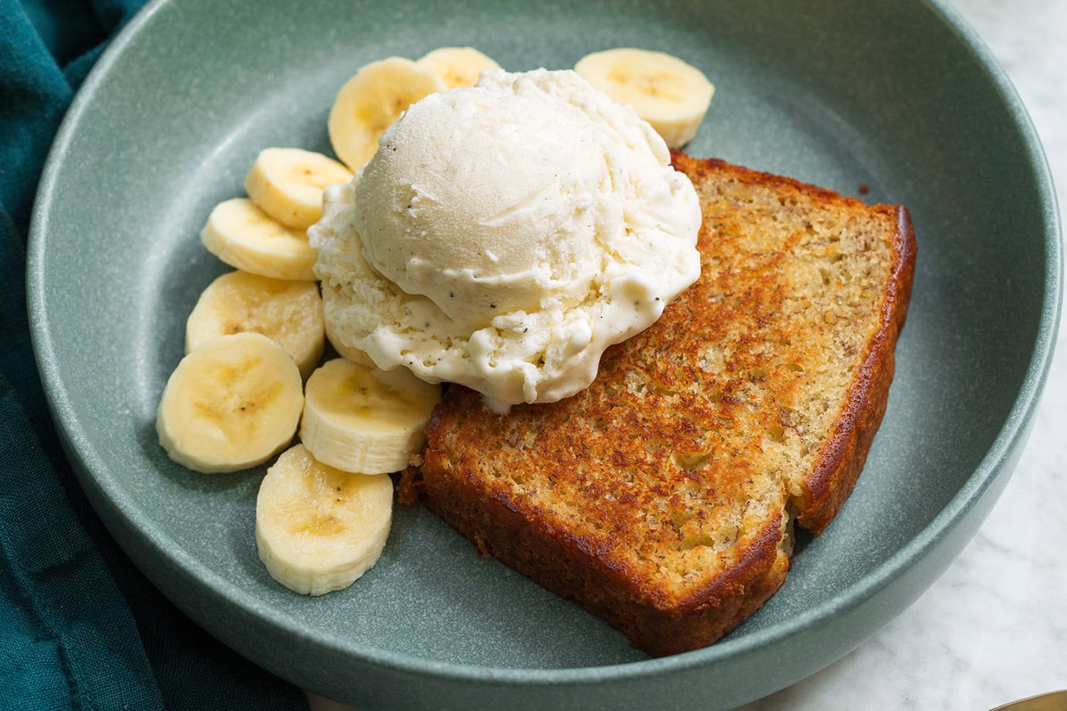 Toasted banana bread layered with a scoop of vanilla ice cream and banana slices to the sides. Showing how to assemble a banana bread sundae.